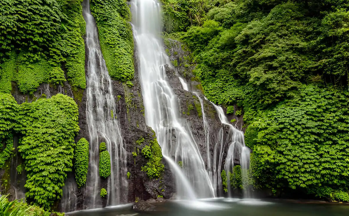 A majestic waterfall cascades down a rocky wall adorned with vibrant green foliage, creating a serene natural escape in Bali’s lush landscape.