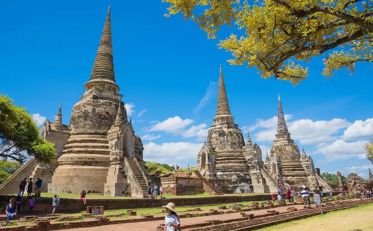 View of the three iconic chedis at Wat Phra Si Sanphet in Ayutthaya Historical Park, surrounded by visitors exploring the ruins on a bright, sunny day.