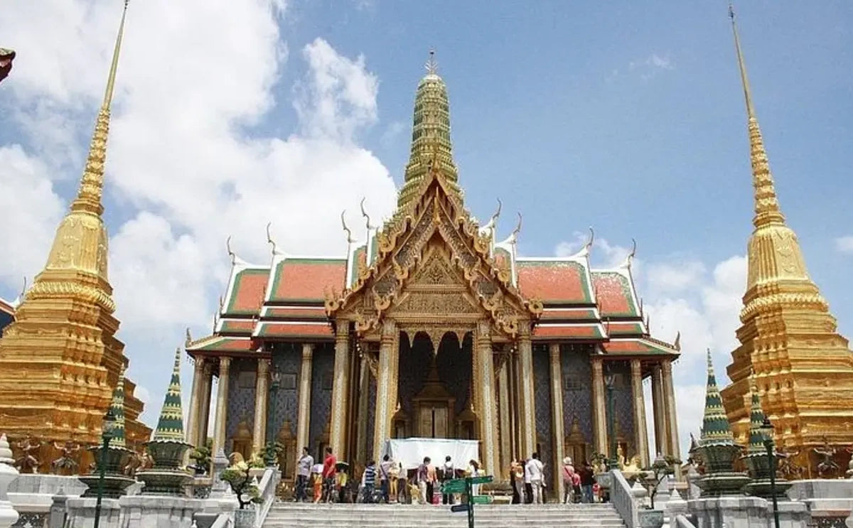 Front view of the Temple of the Emerald Buddha at the Grand Palace in Bangkok, surrounded by golden stupas and intricate architectural details, with visitors exploring the site.