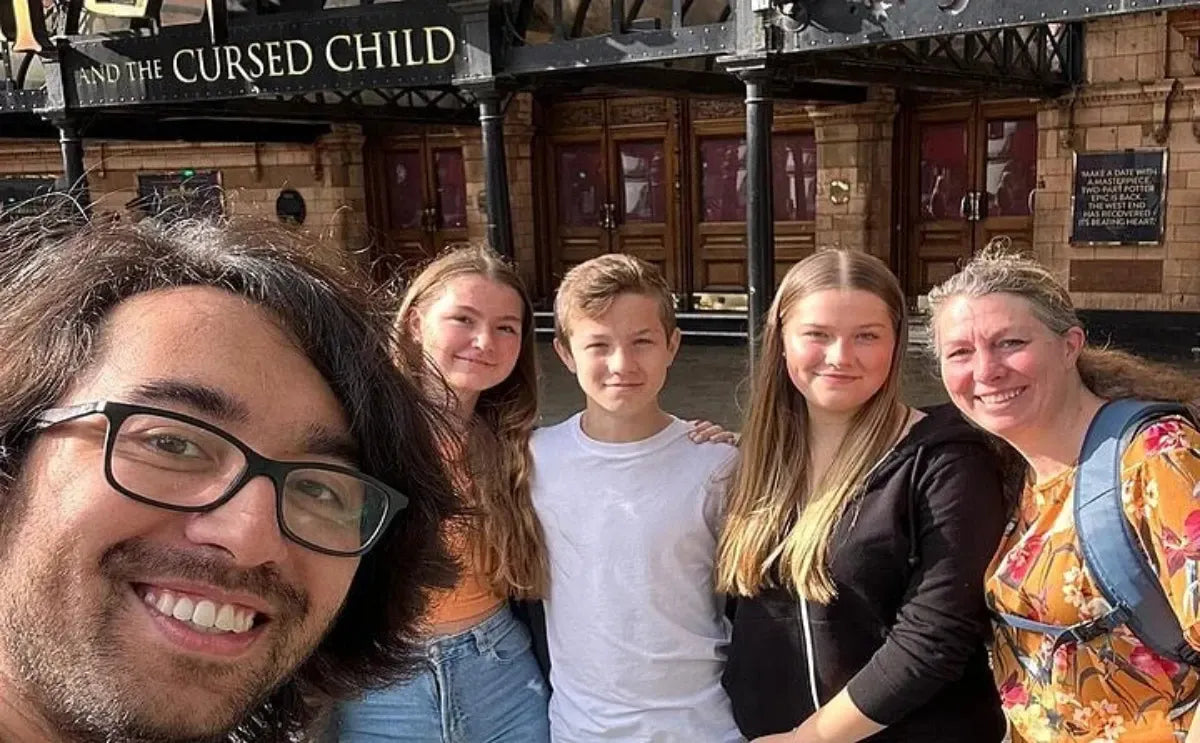 A smiling group of people posing outside a theater in London displaying a Harry Potter-themed play, capturing a fun moment from their tour.
