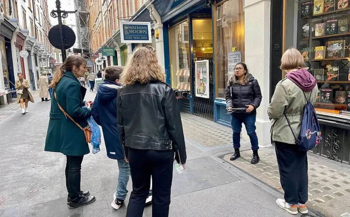 A guide leading a small group through a narrow London street, pointing out Harry Potter-related spots near a bookstore with themed displays.