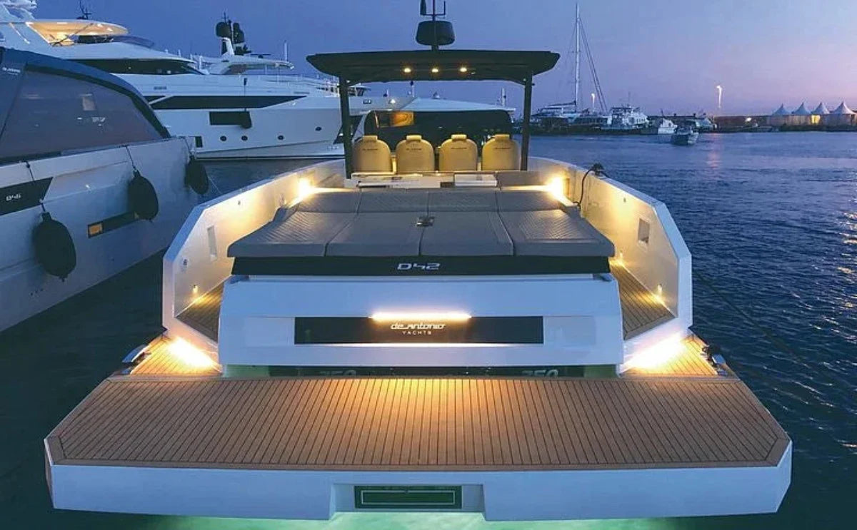 A sleek motor yacht, "Para Voce," docked at a marina during twilight, illuminated by soft onboard lighting. The spacious full-width swim platform and lounge areas are highlighted, surrounded by calm waters and neighboring yachts.