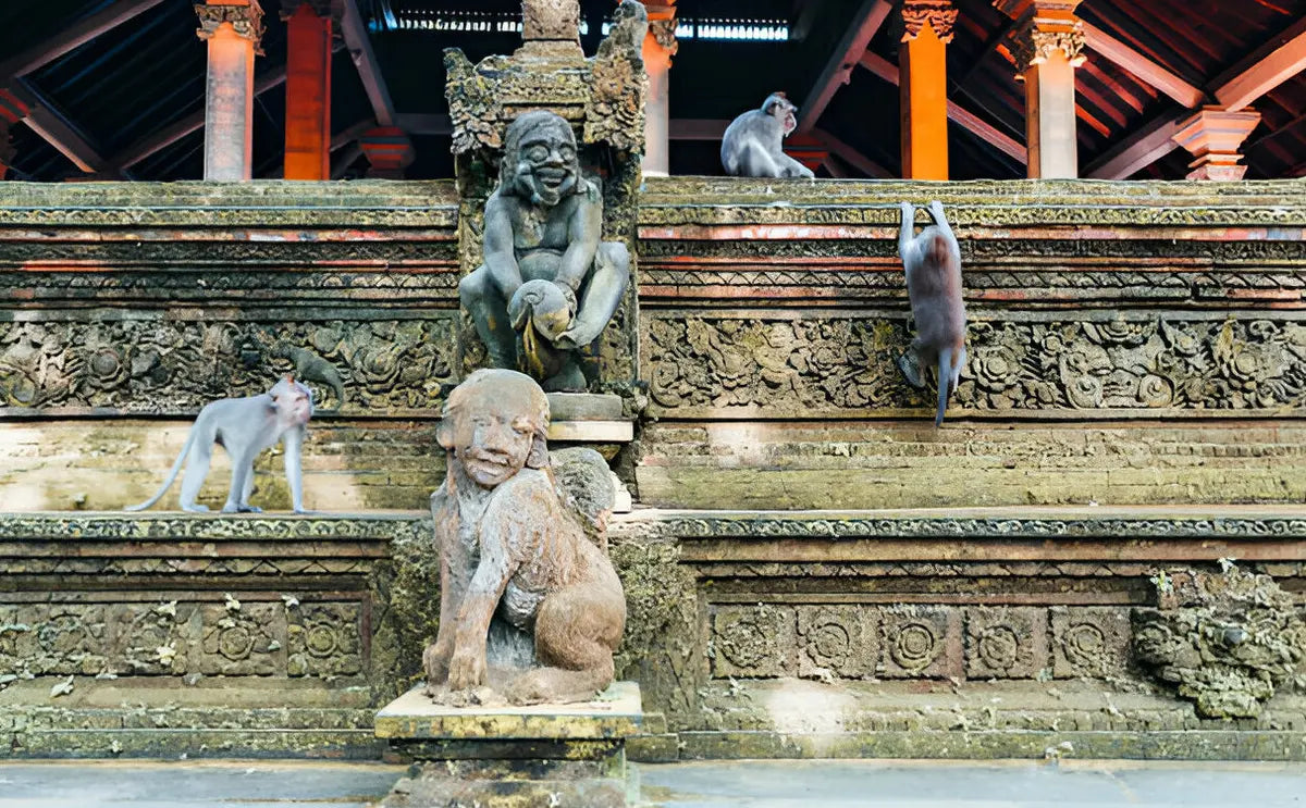 Monkeys climbing and exploring ancient stone carvings and statues inside the Monkey Forest Sanctuary in Bali.