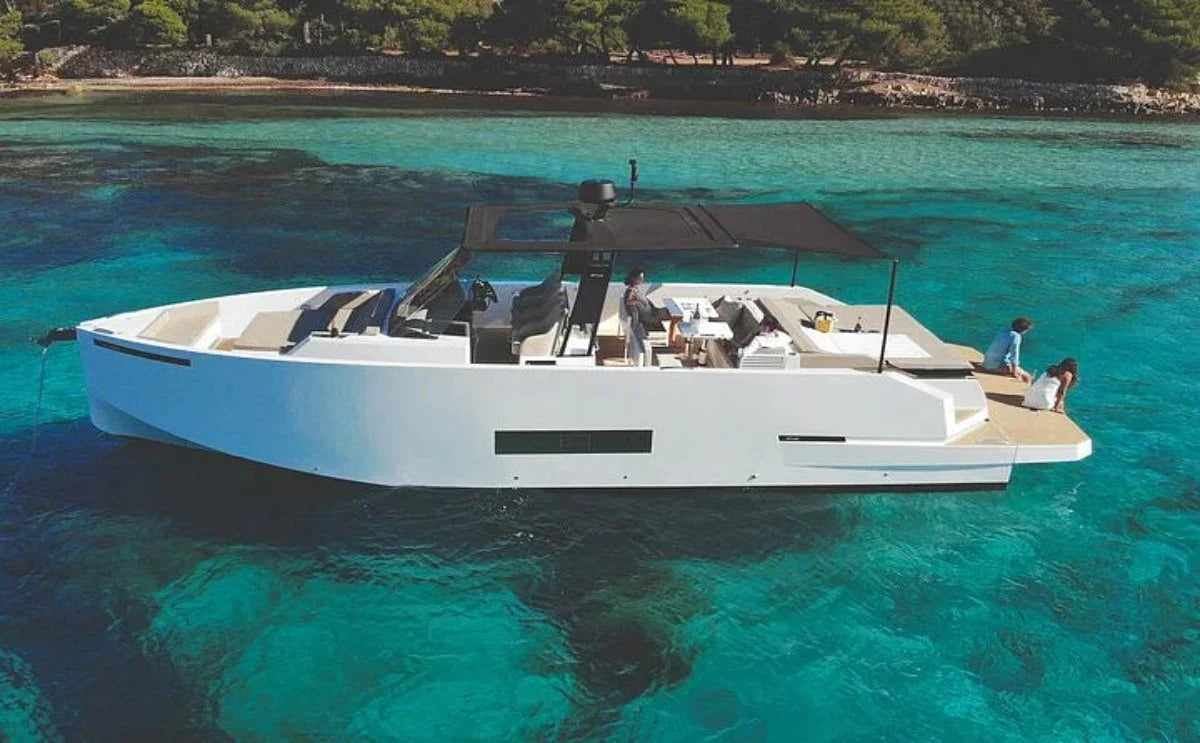 A sleek motor yacht anchored in turquoise waters. Guests relax on the deck, enjoying the peaceful setting with a scenic coastline and lush greenery in the background.
