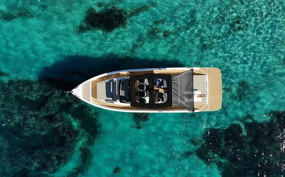 An aerial view of a luxury motor yacht floating in crystal-clear turquoise waters. The spacious deck layout and sleek design are highlighted, surrounded by the serene beauty of the sea.
