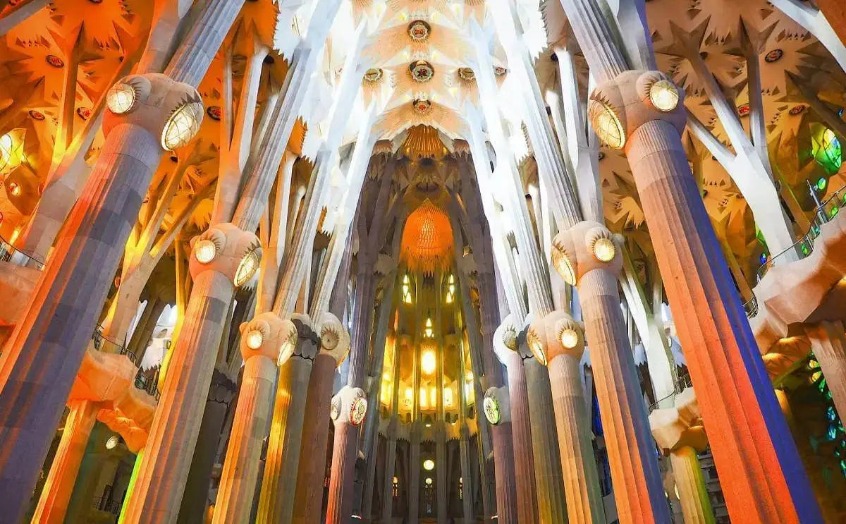 Interior view of the Sagrada Família showcasing tall illuminated columns, vibrant stained-glass windows, and intricate architectural details.