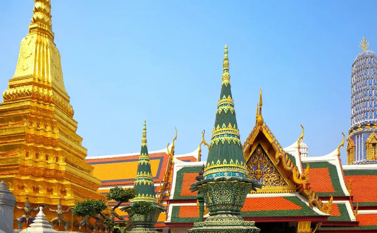 Close-up of the ornate structures at the Temple of the Emerald Buddha, featuring a golden stupa, colorful spires, and detailed rooftops within the Grand Palace complex.