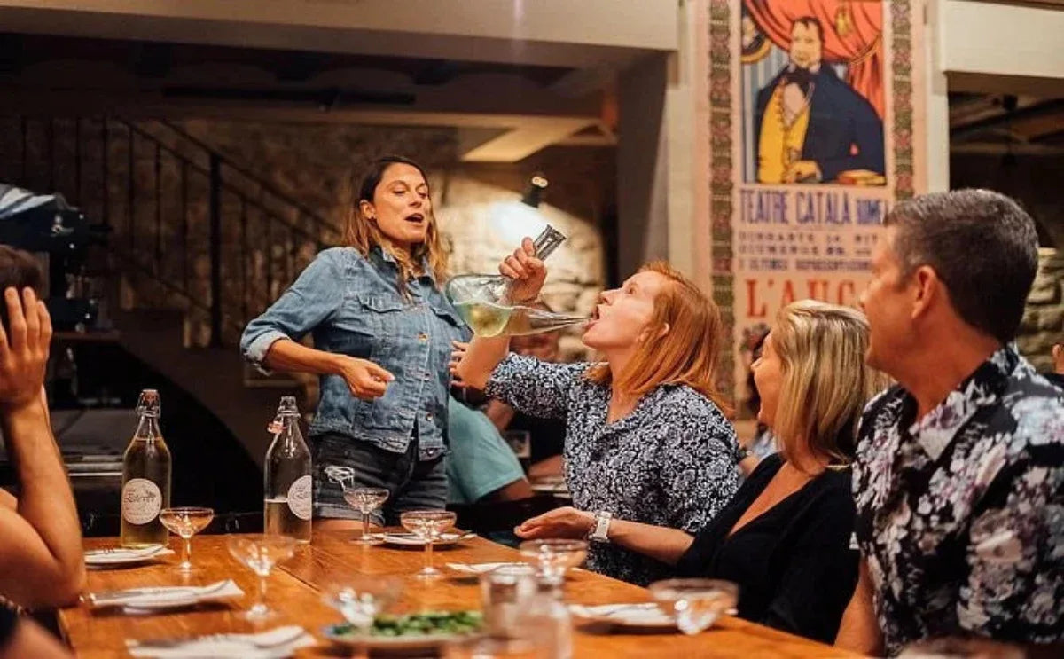 A lively moment during a tapas tour in Barcelona, where guests engage in traditional wine-drinking practices while enjoying a fun and interactive dining experience.
