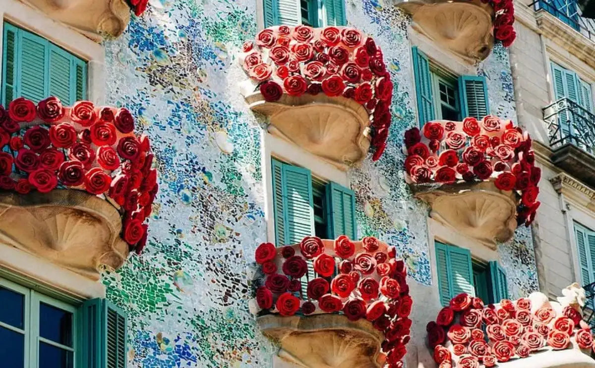 The colorful façade of Casa Batlló in Barcelona, adorned with intricate mosaics and striking red floral decorations on its balconies, captures the playful and innovative spirit of Gaudí's architectural style.