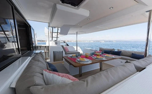 A luxurious catamaran docked on calm waters with a spacious lounge area featuring comfortable seating and a dining table set with colorful dishes, offering a perfect setting for a relaxing cruise.