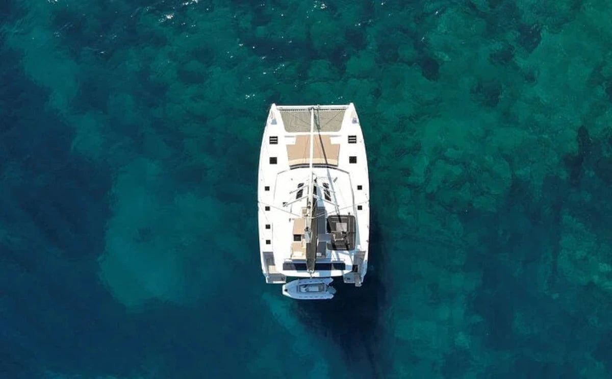 Aerial view of the "White Coral" catamaran anchored in crystal-clear turquoise waters, showcasing its sleek design and spacious deck.