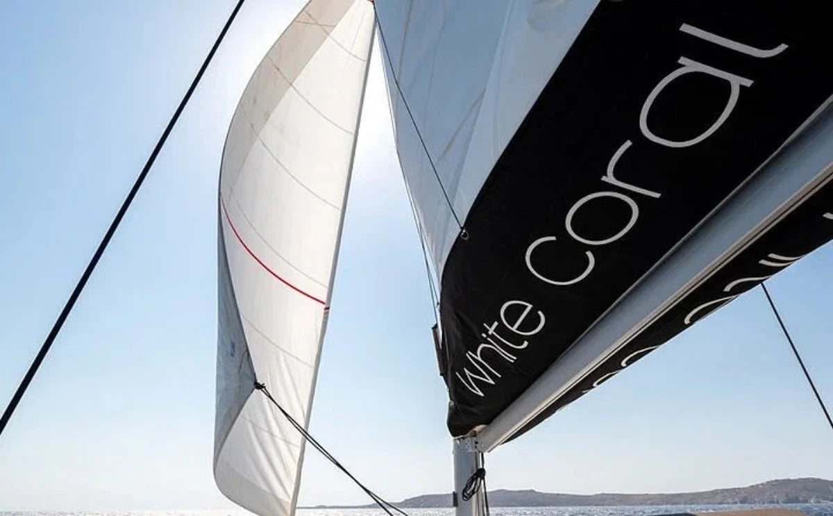 The sails of the "White Coral" catamaran unfurled against a bright sky, gliding smoothly across the sparkling waters of Mykonos.
