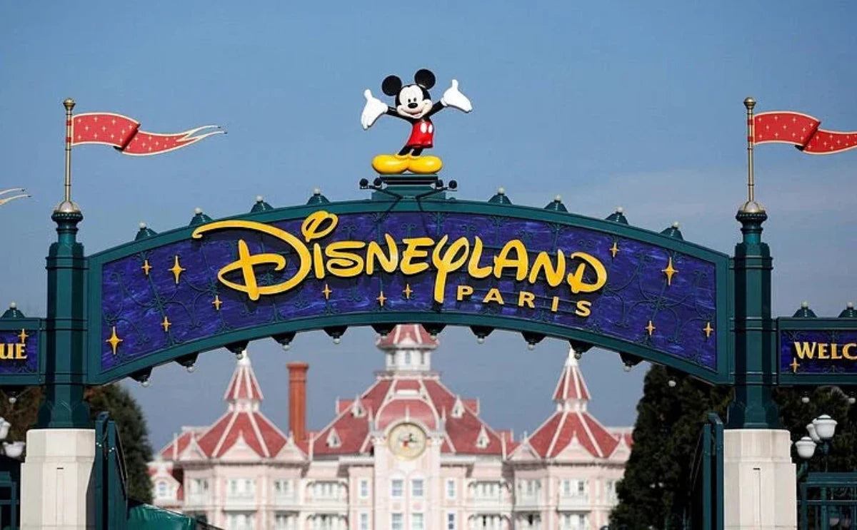 The iconic Disneyland Paris entrance sign, featuring Mickey Mouse, welcomes visitors with the Disneyland Hotel in the background.