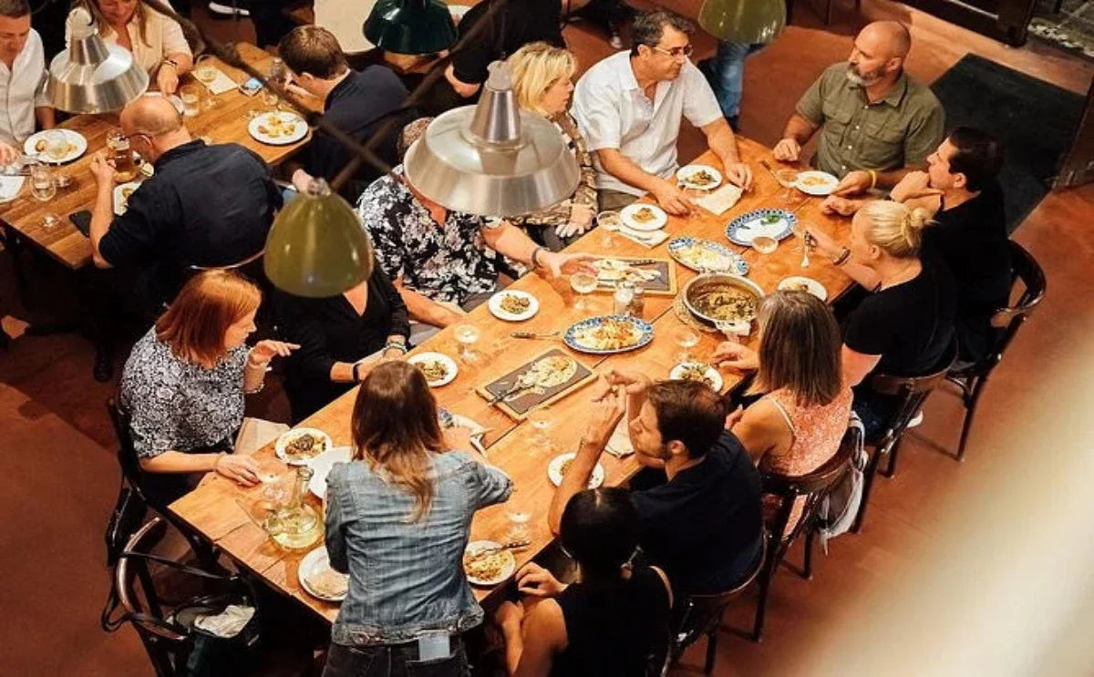 A lively group gathers around a wooden table, enjoying a variety of Catalan tapas and sharing stories during a Barcelona food tour.