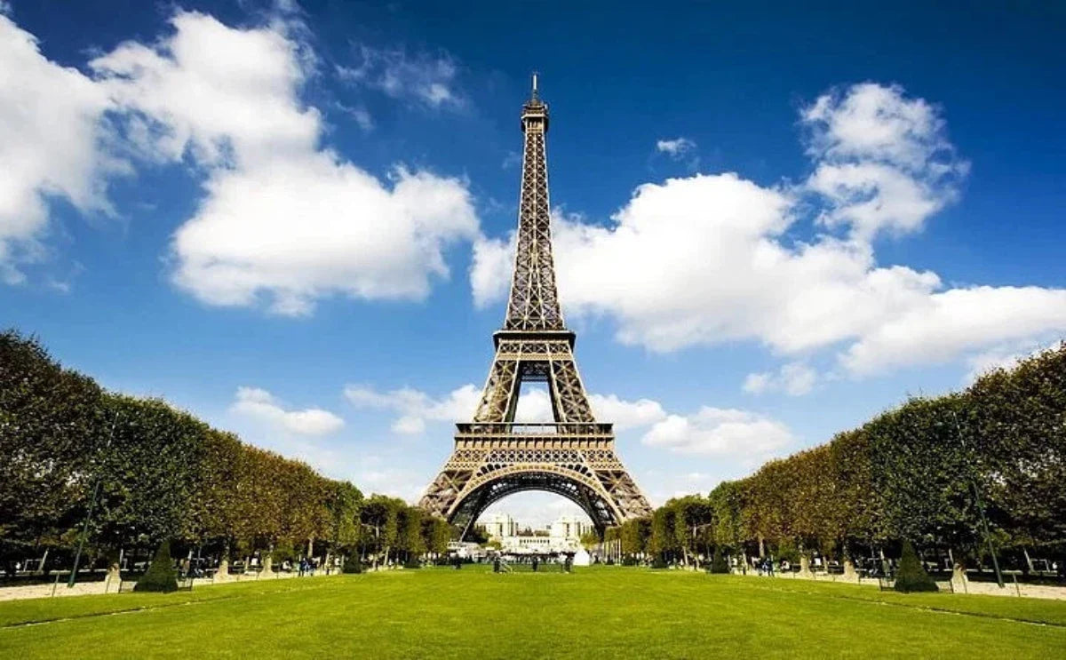 The Eiffel Tower stands tall with clear blue skies and green lawns in the foreground.