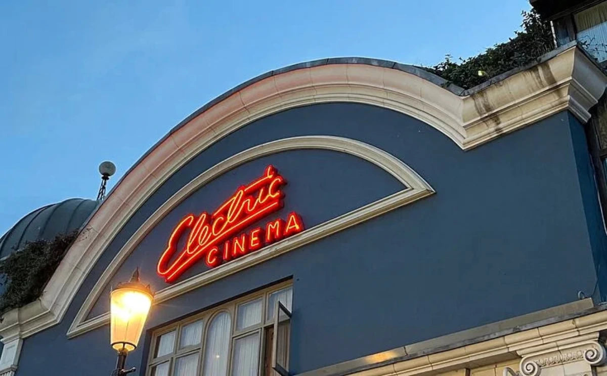 The Electric Cinema building in Notting Hill with its red neon sign glowing on a dark blue façade under a clear sky.