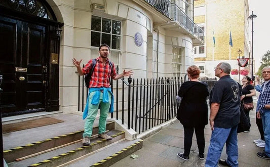 A guide speaking to a group of tourists outside a building, likely associated with Beatles history, while gesturing animatedly near a staircase marked for safety.