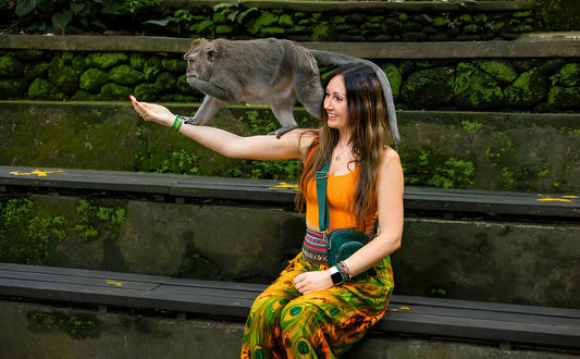 Tourist smiling as a monkey climbs onto her arm at the Monkey Forest in Bali, surrounded by green plants and stone steps.