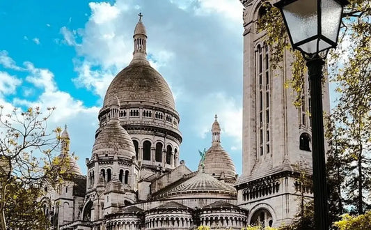 Front view of Sacré-Cœur Basilica with a lamppost in the foreground and trees on a clear day.