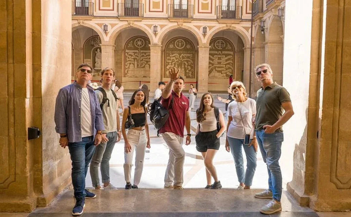 A tour group listens attentively to a guide explaining the history and significance of Montserrat Monastery in its impressive courtyard.