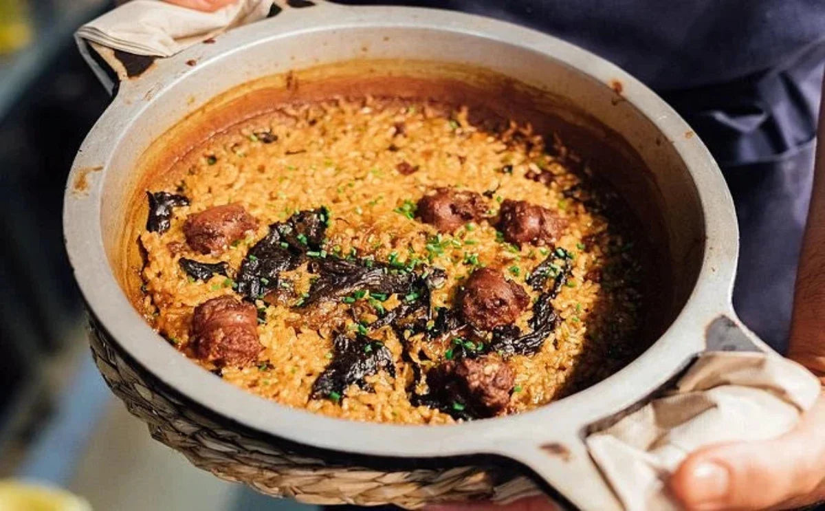 A freshly prepared Catalan-style rice dish served in a traditional clay pot, featuring flavorful local ingredients and garnished with herbs.