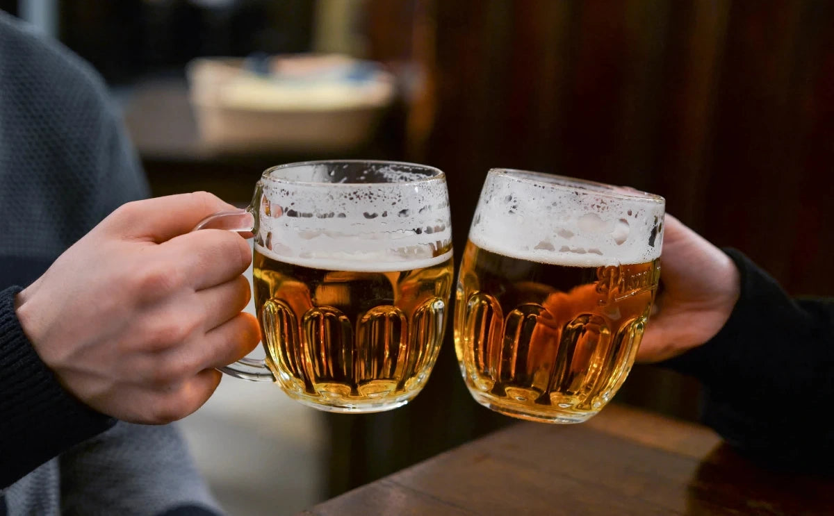Two people clinking glasses of Czech beer in a cozy pub, with clear golden lager and a light frothy head. The dark wooden table and blurred background add to the relaxed atmosphere of a Prague beer walk.