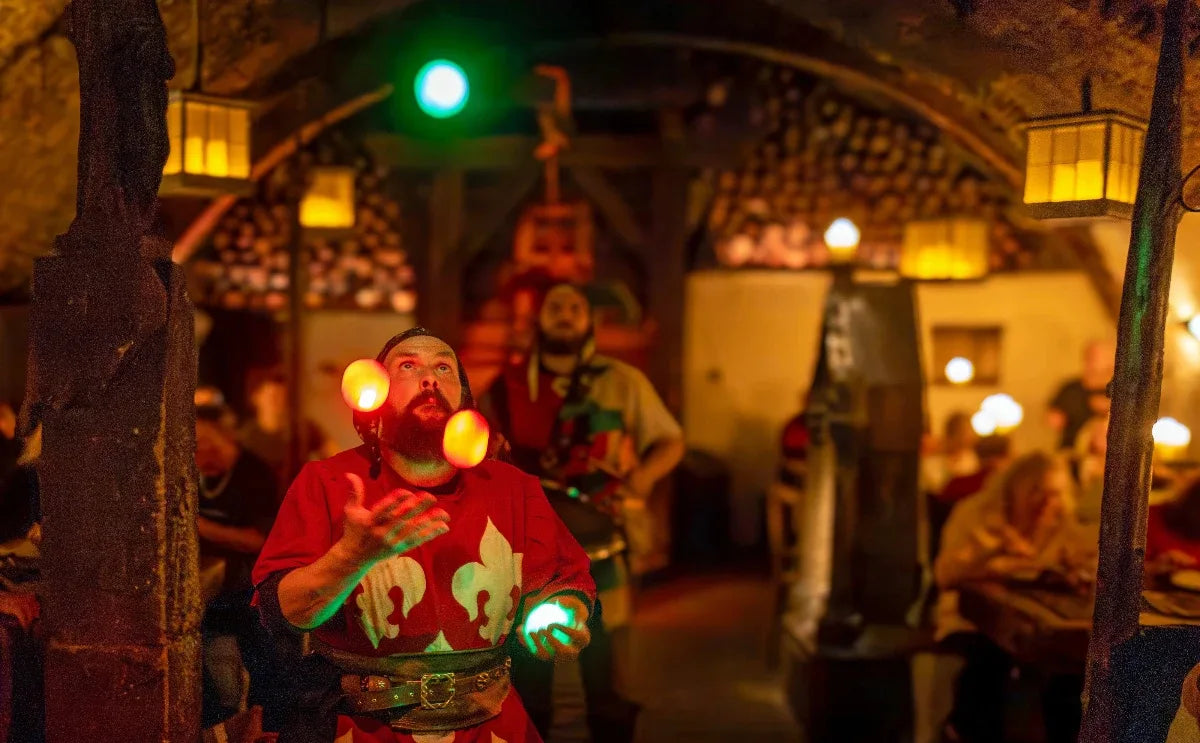 A performer in medieval attire juggling glowing balls inside a dimly lit medieval tavern at Dětenice, with guests dining in the background and rustic decor enhancing the historical ambiance.