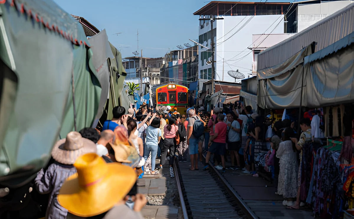 Tourists gathering at the Maeklong Railway Market to watch a train passing through the narrow market street, as vendors quickly retract their awnings and displays to make way.