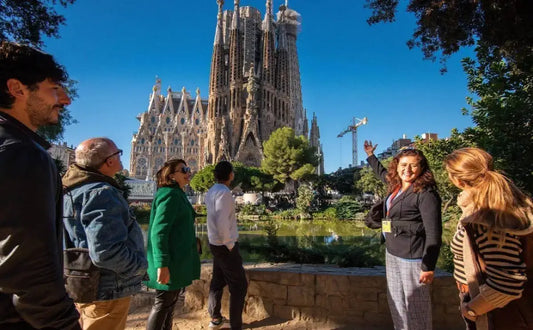 Tour group with a guide pointing at the Sagrada Família, highlighting its stunning architecture on a sunny day with clear blue skies.