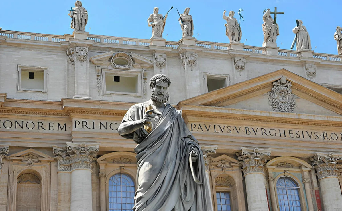 Statue of St. Peter holding keys in front of the facade of St. Peter's Basilica in Vatican City, with detailed architectural features, inscriptions, and statues adorning the building's upper level.