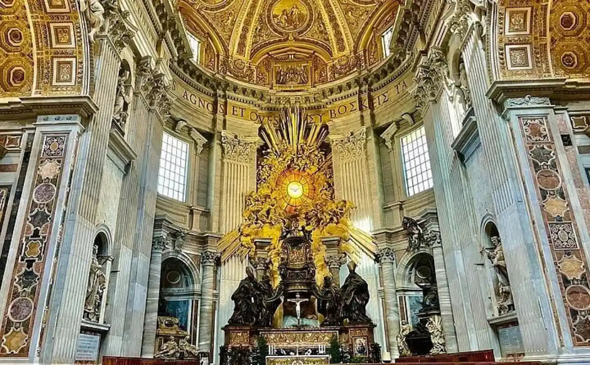 Interior view of St. Peter's Basilica in Vatican City showcasing the ornate architecture, golden dome, and the Altar of the Chair of St. Peter surrounded by dramatic sculptures and vibrant stained glass.