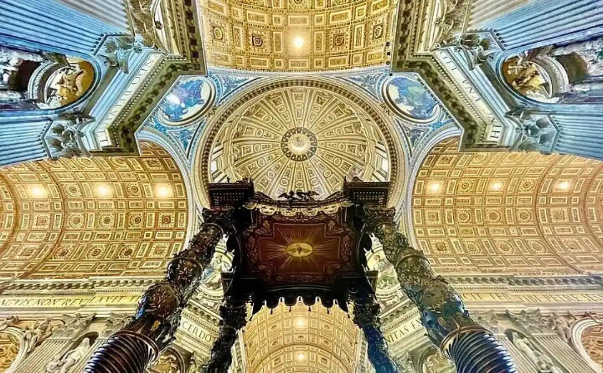 View of the ornate ceiling and dome interior of St. Peter's Basilica, featuring intricate golden designs, vibrant mosaics, and Bernini's bronze Baldachin in the foreground.