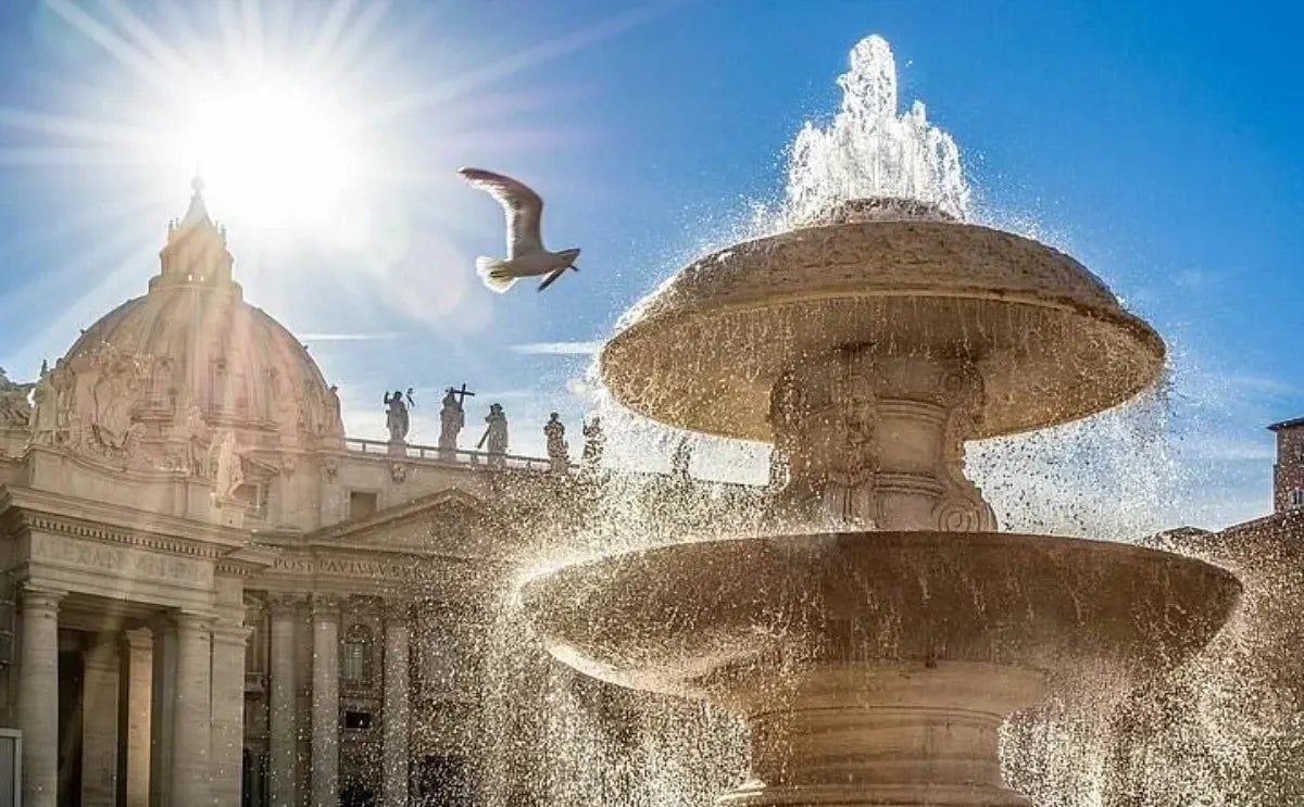 Fountain in St. Peter's Square with water cascading under bright sunlight, a bird in flight, and the dome of St. Peter's Basilica in the background.