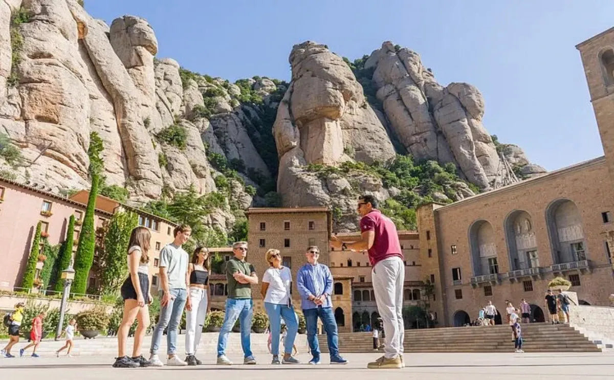 A guide shares insights with a group of visitors in the main square of Montserrat Monastery, framed by the rugged rock formations of the surrounding mountain.